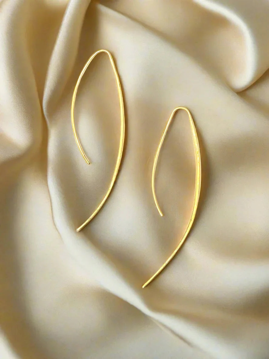 Minimalist long curved gold earrings displayed on soft beige fabric background