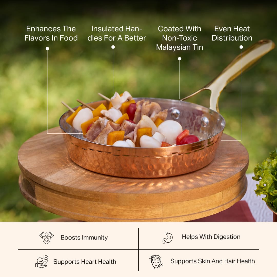 Copper frypan with brass handle, filled with chicken and vegetable skewers, on a wooden stand outdoors.