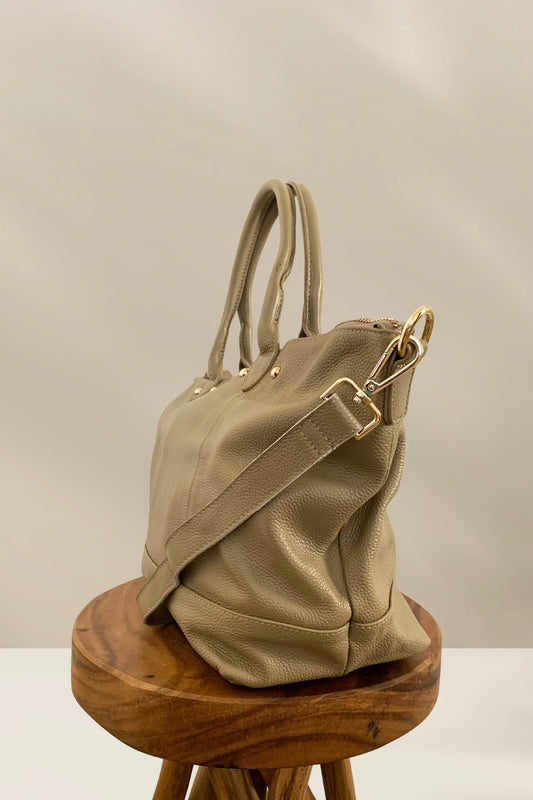 Beige pebbled leather handbag with gold hardware and detachable strap on wooden stool