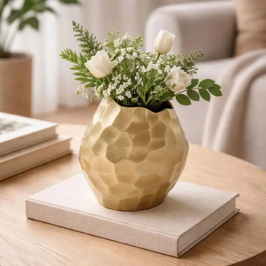 Gold faceted aluminum vase styled with white roses and greenery on a wooden coffee table in a modern living room
