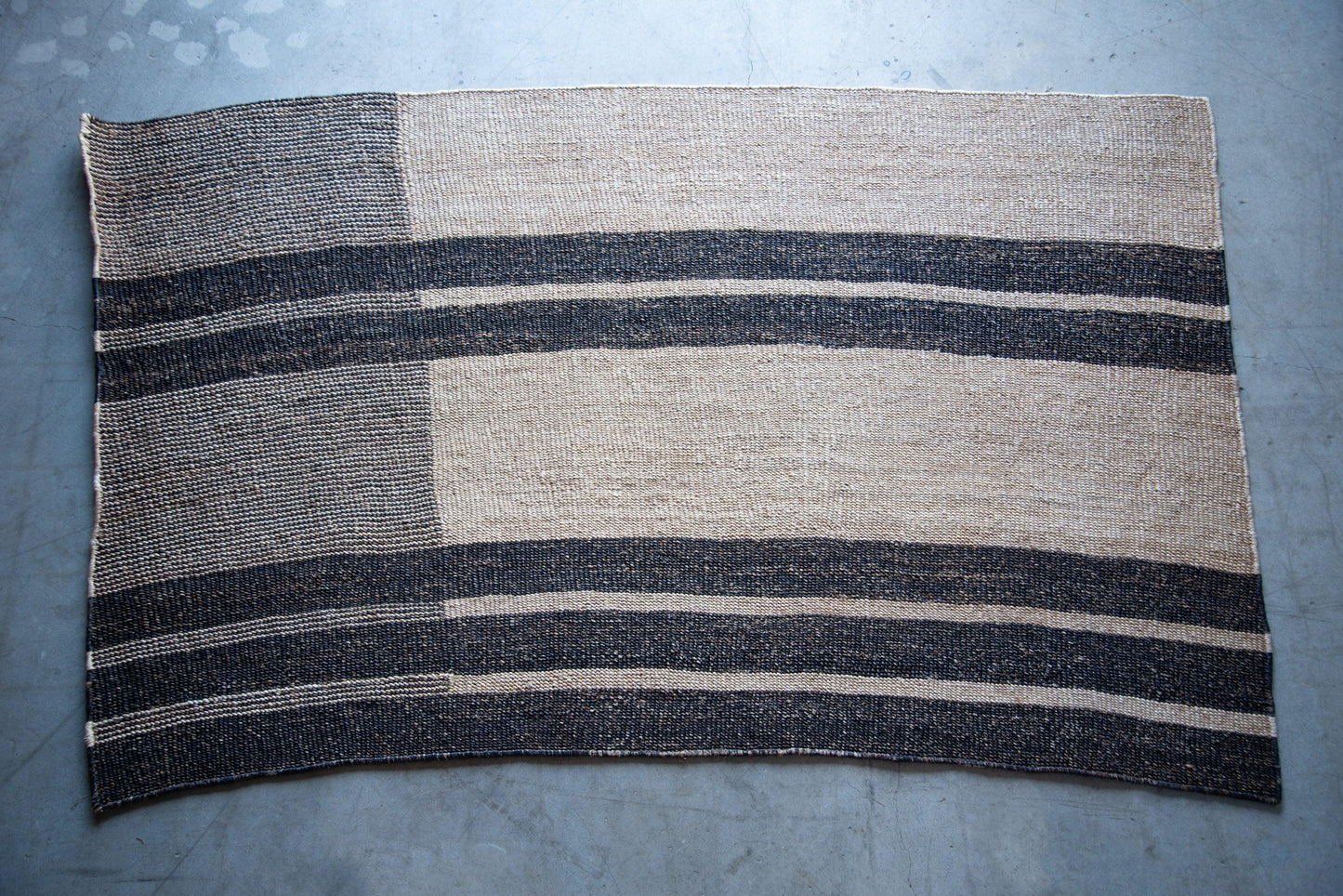Full flat lay of handwoven rectangular sisal rug tea black variant showing asymmetric block stripe pattern cream field charcoal stripes