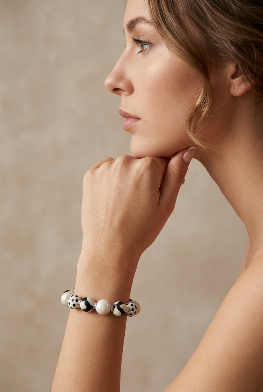 Model wearing a Sefone artisan bracelet with cream and patterned black-and-white clay beads, resting her hand beneath her chin.