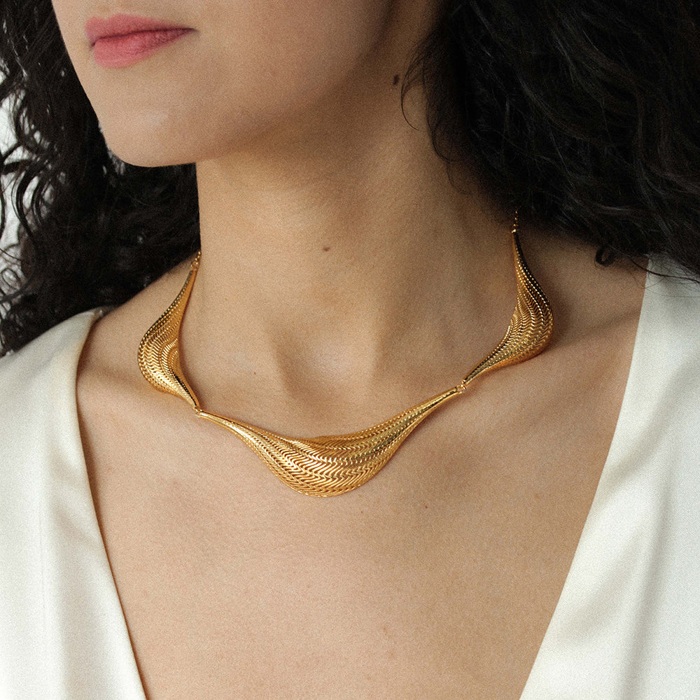 Model with dark wearing a structured gold-tone woven mesh collar necklace and a white top
