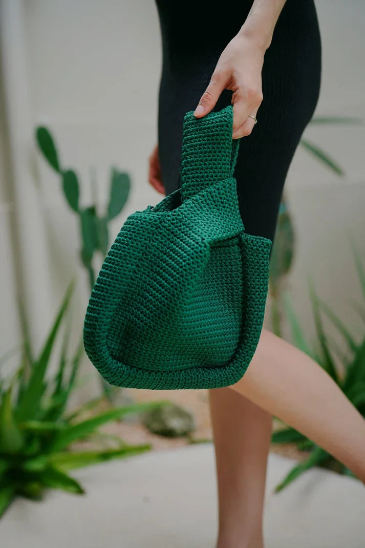 Forest green woven artisan clutch bag held against botanical backdrop — Handcrafted Clutches Collection — Fluent Trends