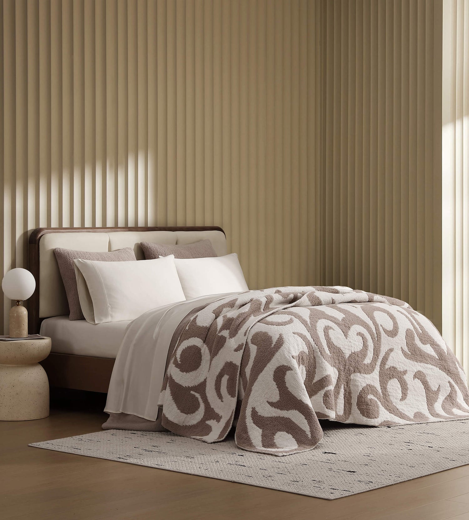 Mocha brown plush textured throw blanket folded neatly at the foot of a modern upholstered bed with matching pillows in a bright neutral bedroom lifestyle view