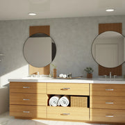 Modern bathroom vanity with light wood cabinets, double sinks, round mirrors, and rolled towels