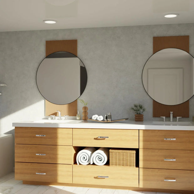 Modern bathroom vanity with light wood cabinets, double sinks, round mirrors, and rolled towels