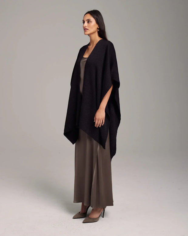 Woman wearing a black knitted poncho over a taupe satin maxi dress with gray high heels