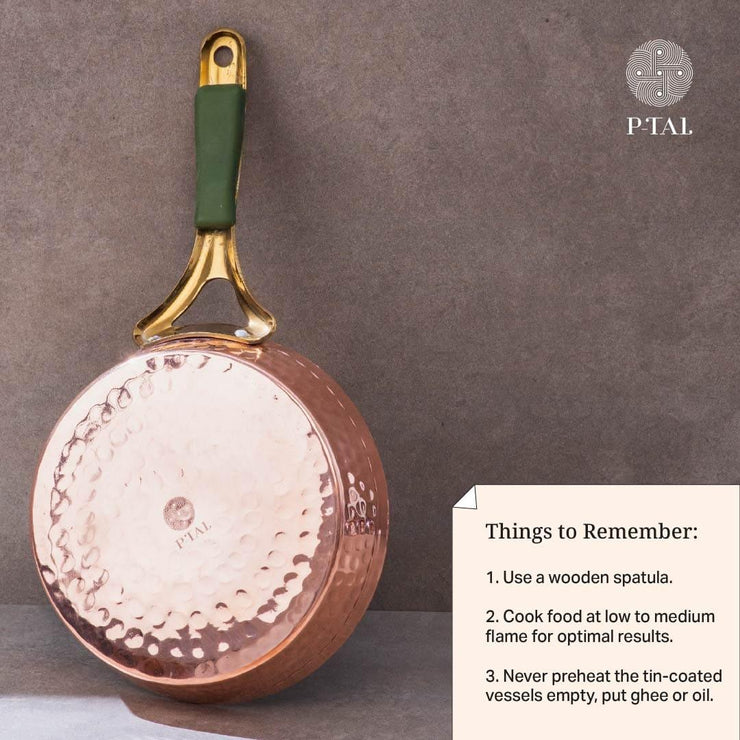 Copper frypan showing its hammered bottom, brass handle with green grip, and care instructions card. P-TAL brand logo.