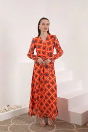 Woman in long red patterned maxi dress with belt, standing in minimalist indoor setting