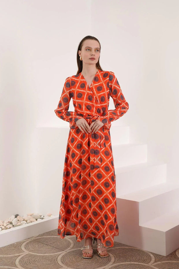 Woman in long red patterned maxi dress with belt, standing in minimalist indoor setting
