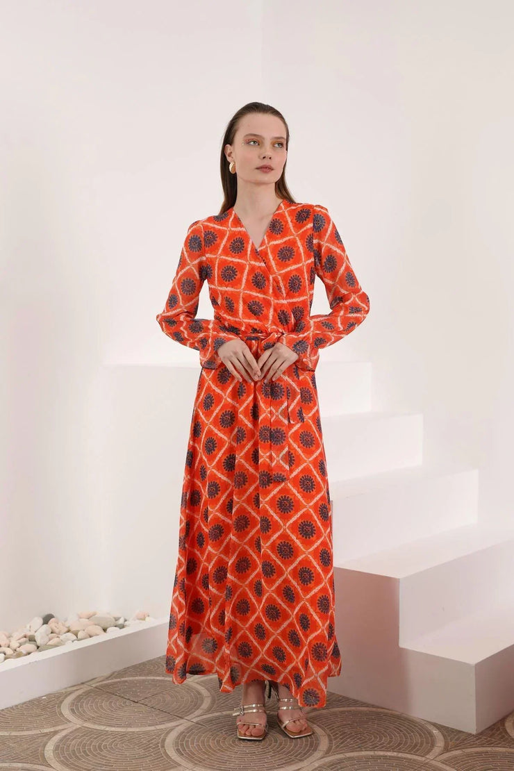Woman in long red patterned maxi dress with belt, standing in minimalist indoor setting