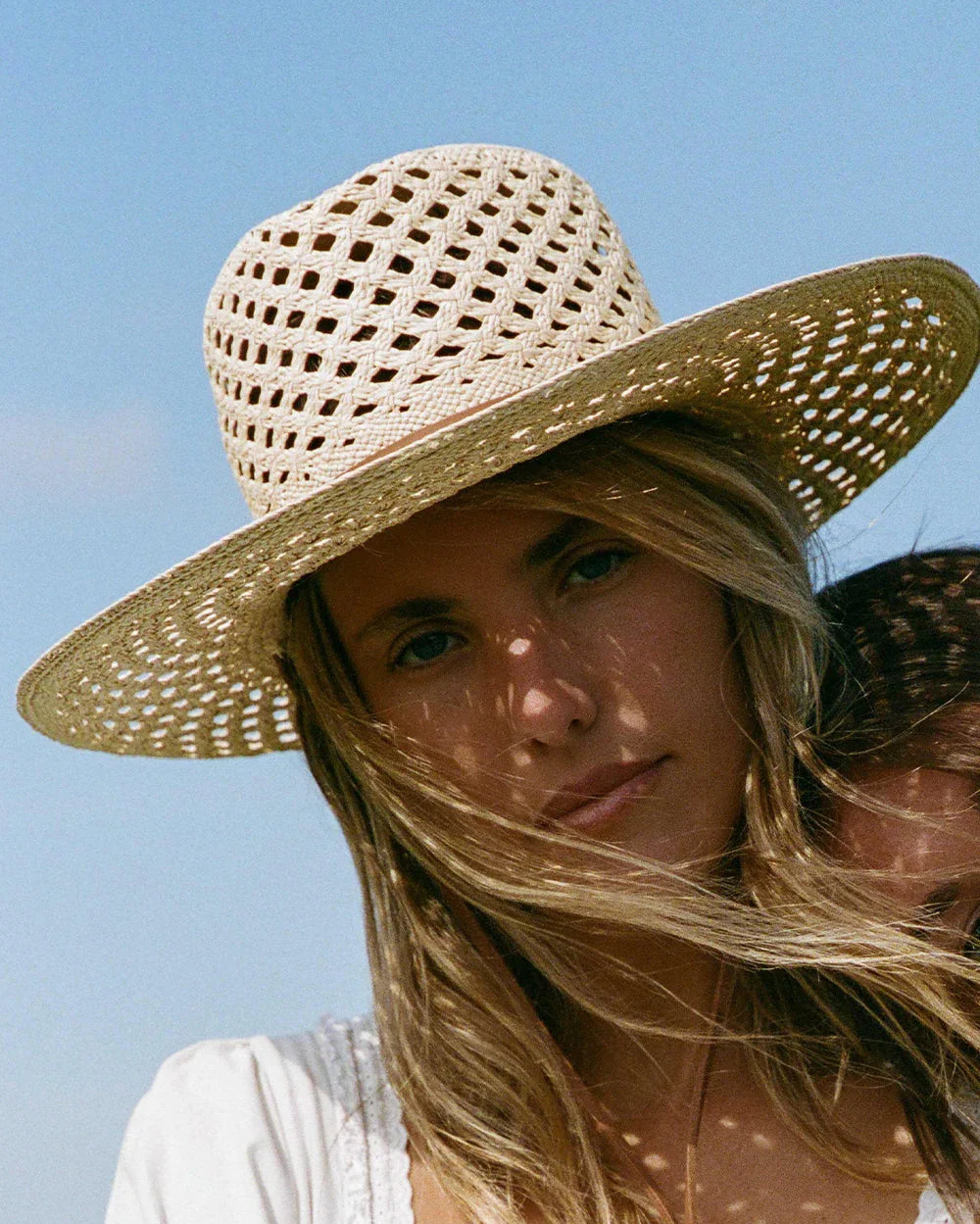 Close-up of woman wearing a stylish woven straw hat with a white blouse against a blue sky