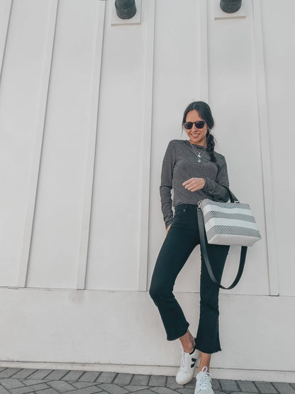 Woman wearing striped long-sleeve top, black cropped jeans, white sneakers, sunglasses, and holding black and white striped shoulder bag
