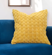 Textured yellow throw pillow on blue velvet sofa with white wall decor