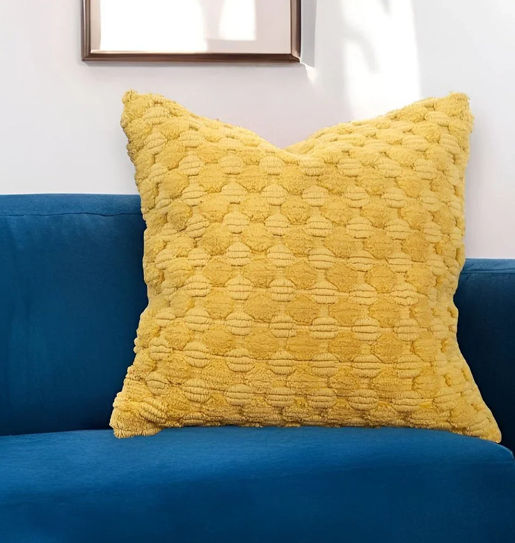 Textured yellow throw pillow on blue velvet sofa with white wall decor