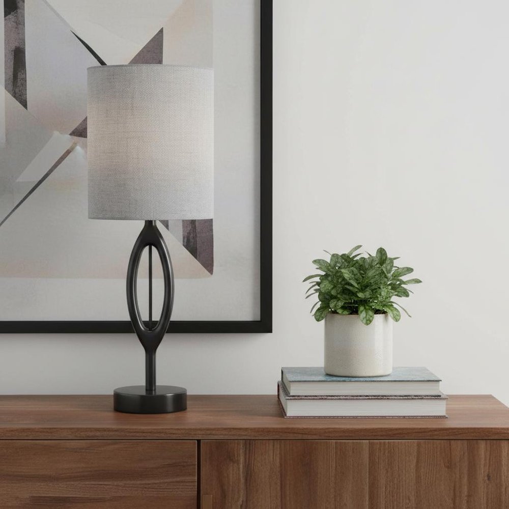Modern 28-inch black wood table lamp with a gray drum fabric shade and sculpted oval base on a wooden sideboard.