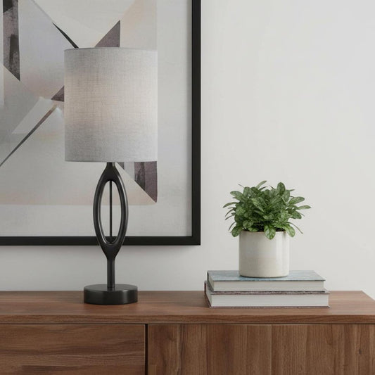 Modern 28-inch black wood table lamp with a gray drum fabric shade and sculpted oval base on a wooden sideboard.