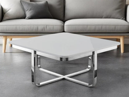 Modern square coffee table with chrome legs and glossy white top in front of grey sofa