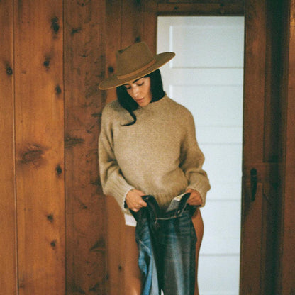 Woman in beige sweater and hat holding blue jeans in rustic wooden room