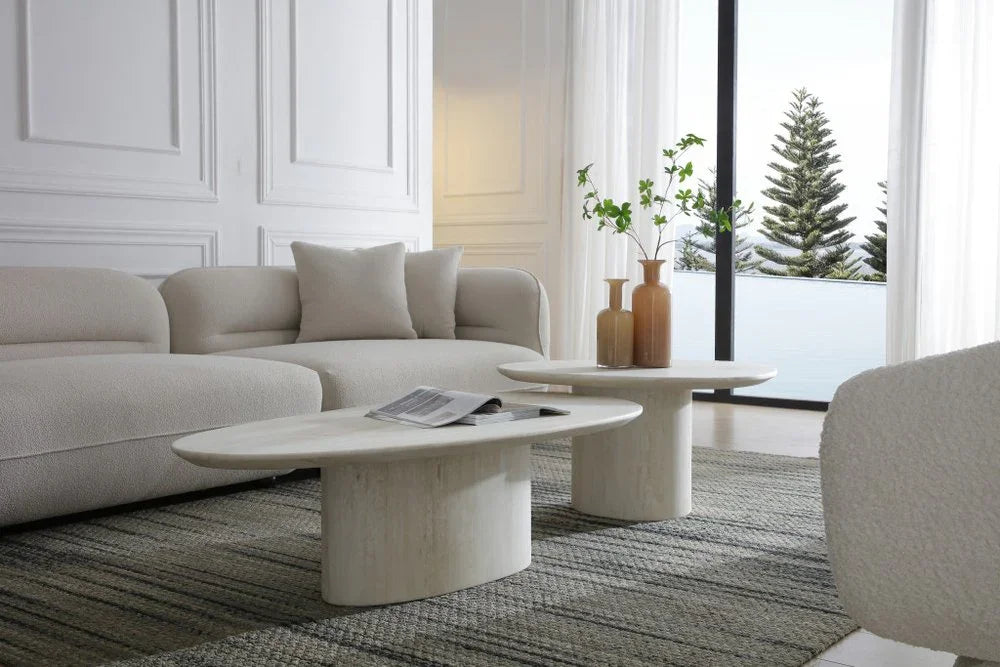 Lifestyle view of the Sia 51-inch beige genuine marble coffee table in a contemporary living room with a matching nesting table, bouclé sofa, and outdoor scenery.