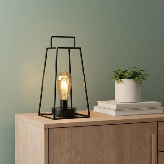 Lifestyle view of a cordless geometric metal lantern with an Edison bulb on a white lace runner, creating a warm glow.