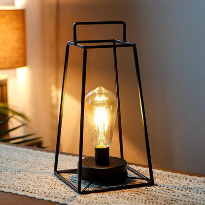 A lit cordless geometric metal lantern showcasing its industrial iron frame and warm Edison bulb in a dim, cozy room setting.