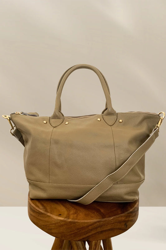 Taupe leather tote bag with gold hardware and adjustable shoulder strap on wooden stool