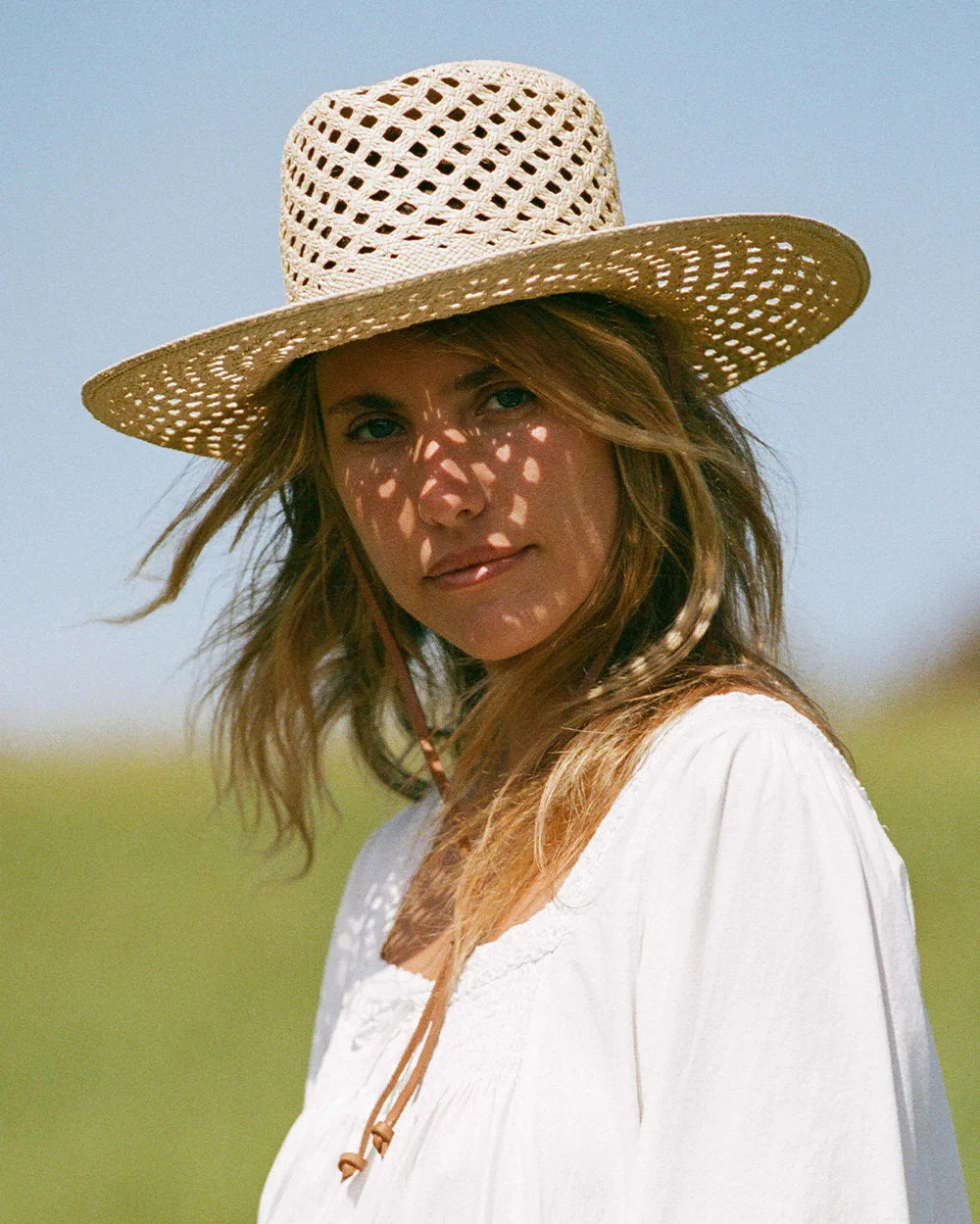 Woman wearing a woven straw hat and white blouse outdoors with shadow patterns on face