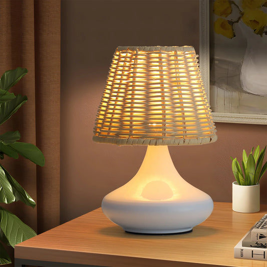 Modern white ceramic table lamp with woven rattan shade on wooden desk with plants and books
