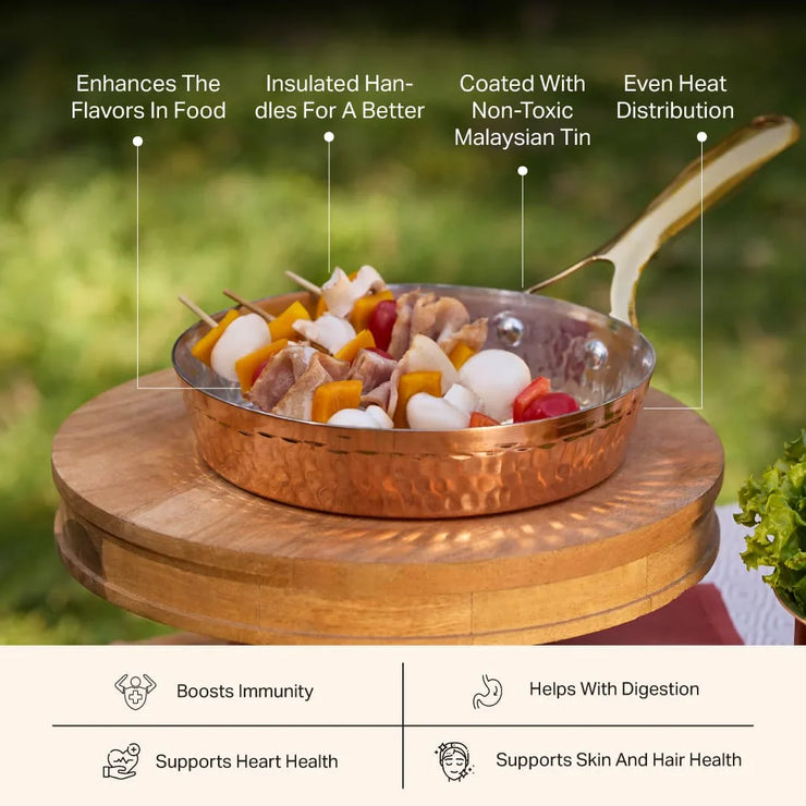 Copper frypan with brass handle, filled with chicken and vegetable skewers, on a wooden stand outdoors.