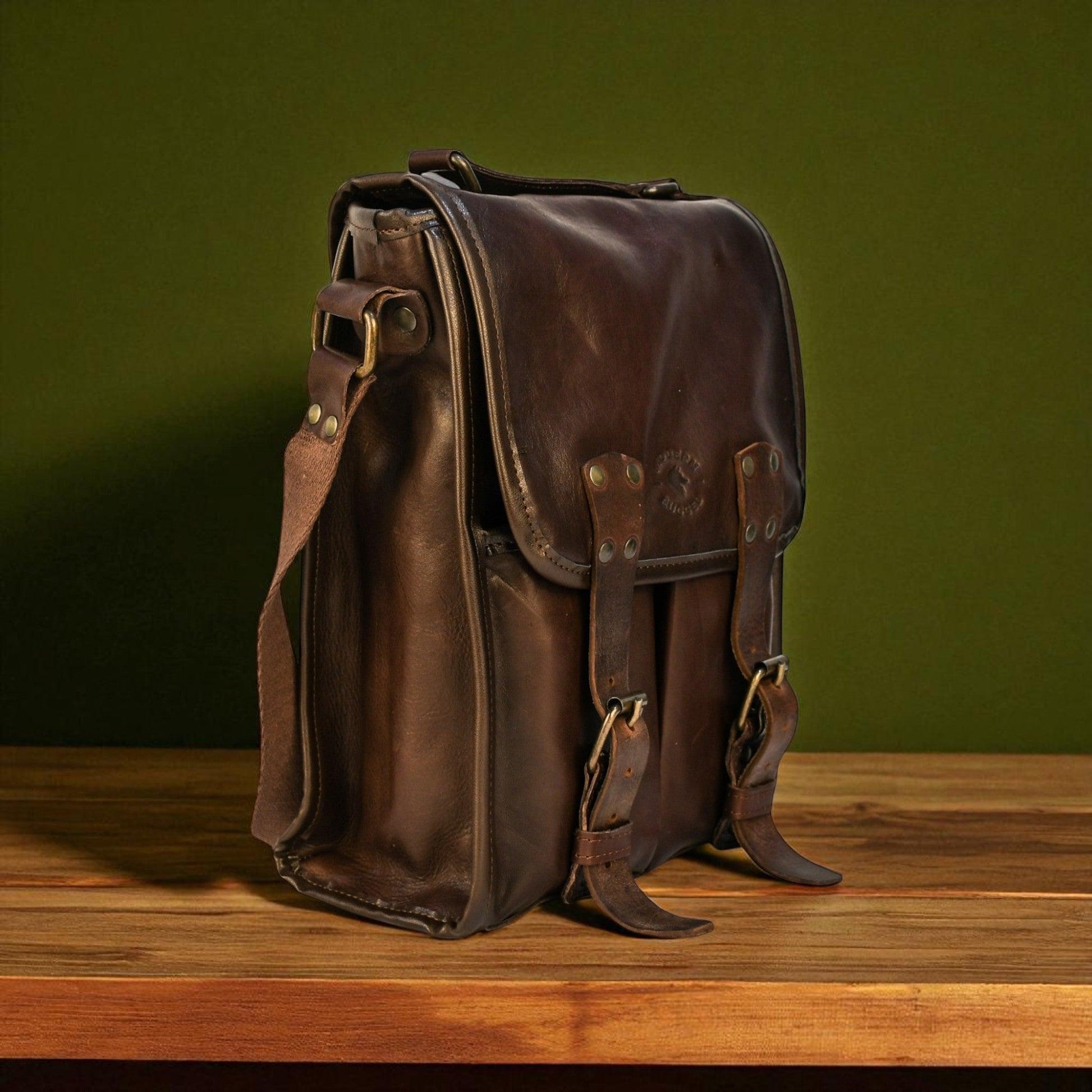 Brown bovine leather medium satchel bag with canvas strap on a wooden surface, showing front buckles and rivets.