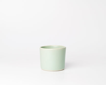 Minimalist light green ceramic cup with a smooth curved rim on white background