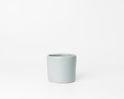 Minimalist light gray ceramic cup with slight uneven rim on white background