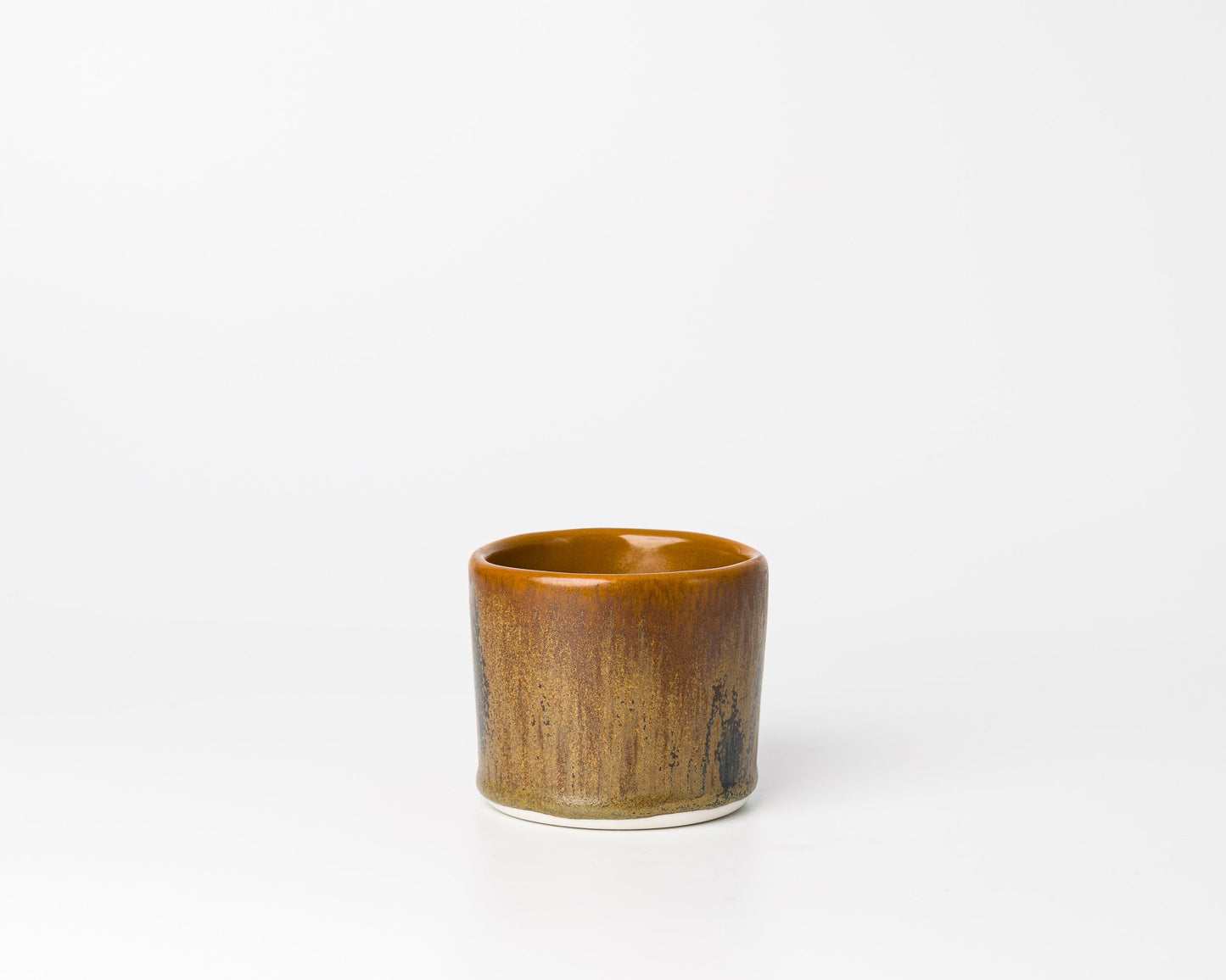 Small brown ceramic cup with rustic glaze on white background