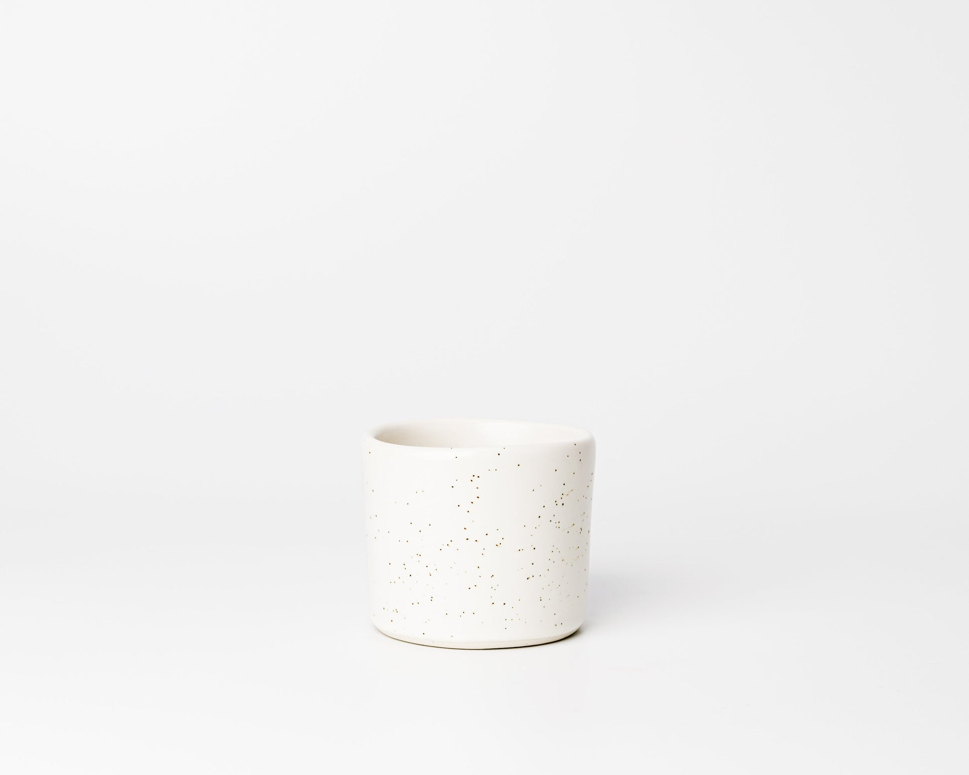 Minimalist white ceramic cup with brown speckles on a white background