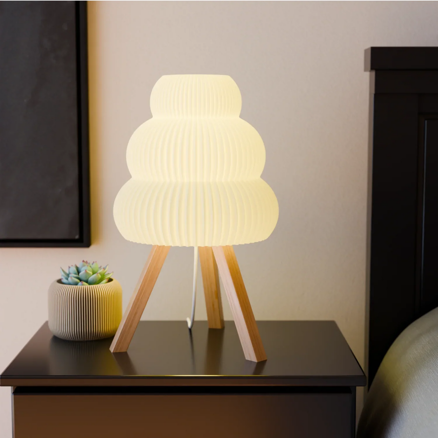 Modern white table lamp with wooden tripod legs on black bedside table next to small succulent pot
