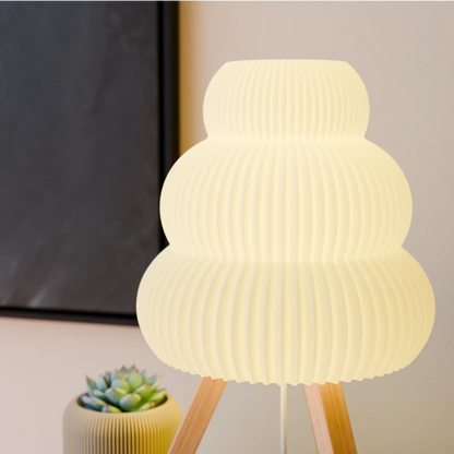 Modern white pleated table lamp on wooden tripod stand next to green succulent plant in ceramic pot