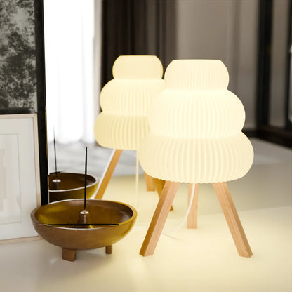 Modern white table lamp with wooden tripod legs and an adjacent wooden incense holder on a light surface
