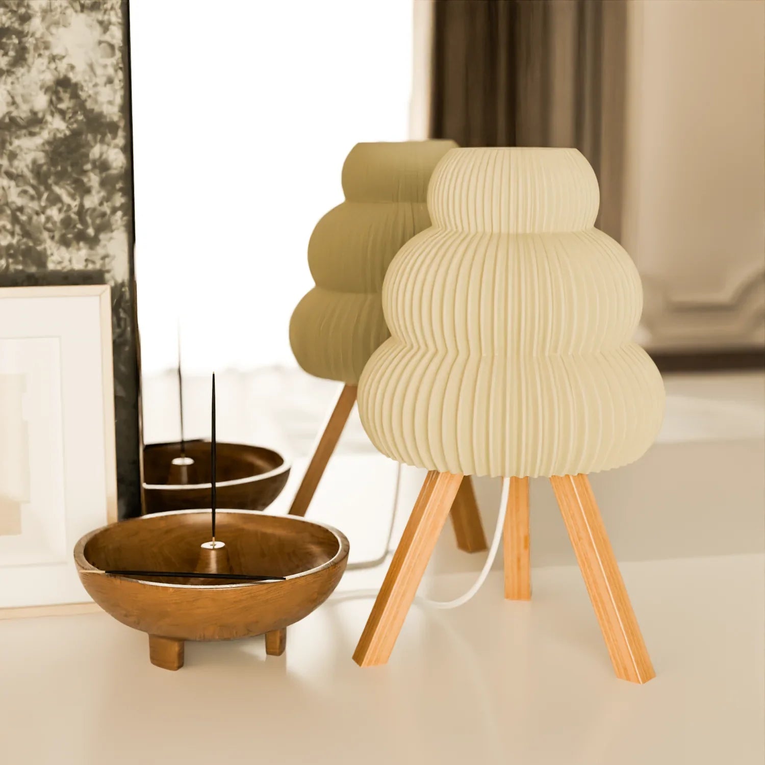 Modern beige table lamp with wooden tripod legs and a wooden bowl with incense stick on white surface