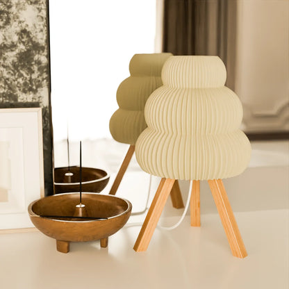 Modern beige table lamp with wooden tripod legs and a wooden bowl with incense stick on white surface