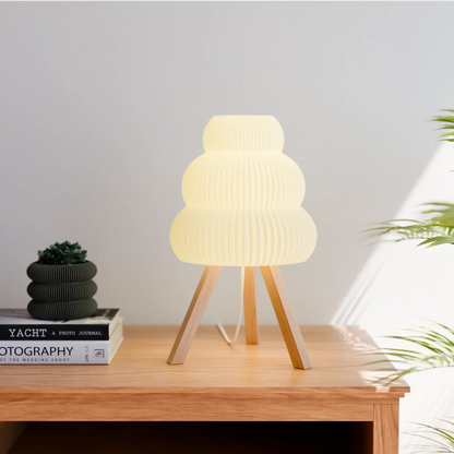 Modern white table lamp with wooden tripod base on light wood side table next to stacked books and small plant