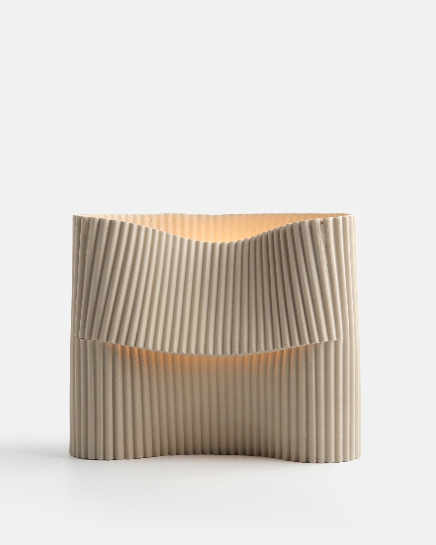 Corduroy handcrafted stoneware table lamp on white background, ribbed sculptural form with warm glow