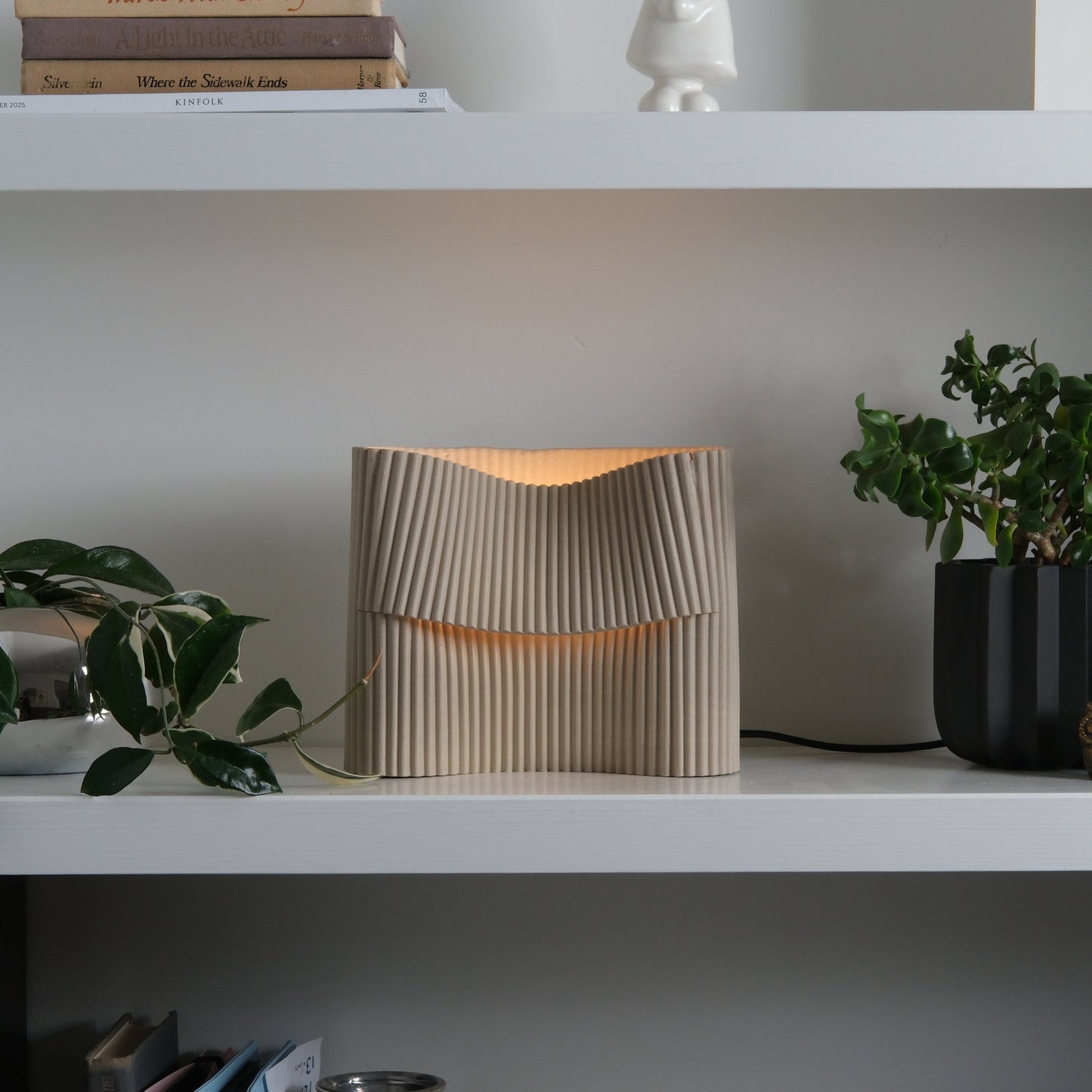 Corduroy table lamp on a white shelf styled with plants and books in a modern interior