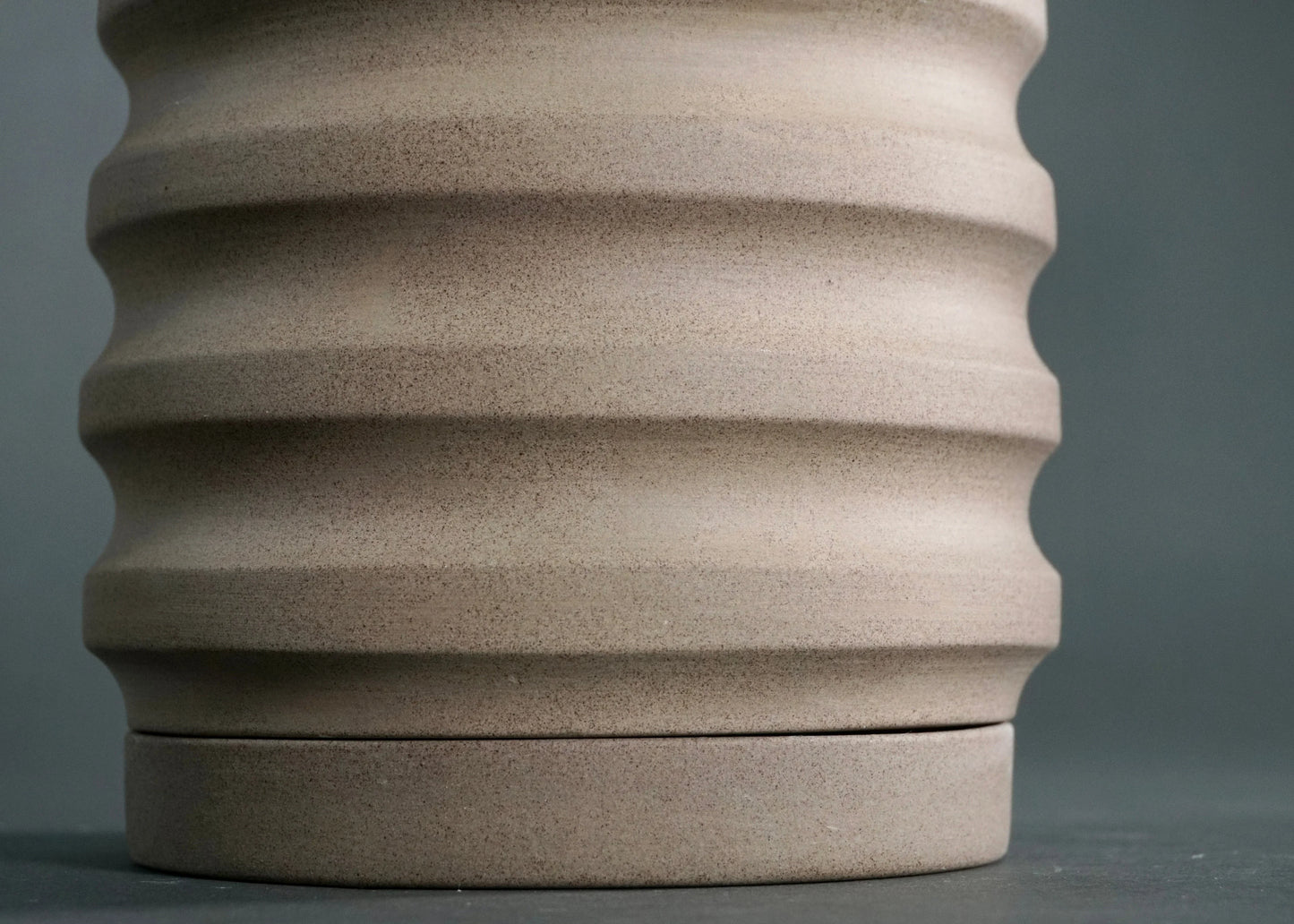 Close-up of a beige ceramic planter pot with horizontal ridges on a gray background