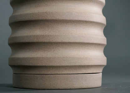 Close-up of a beige ceramic planter pot with horizontal ridges on a gray background