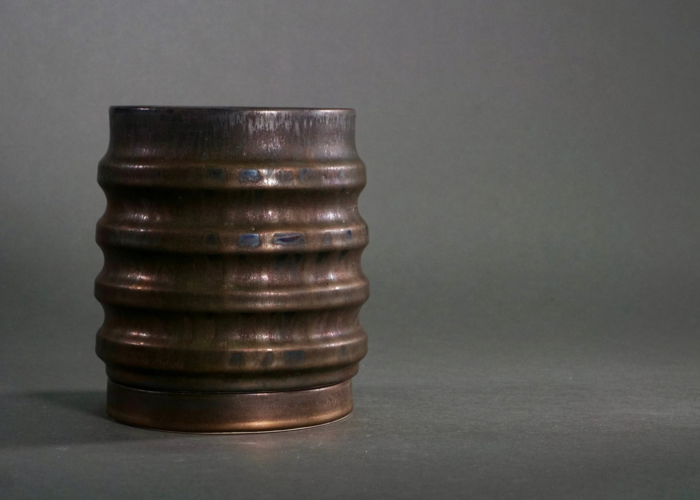 Dark brown ceramic vase with horizontal ridges on gray background