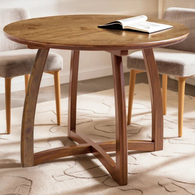 Round wooden dining table with curved legs on a patterned rug, flanked by upholstered chairs