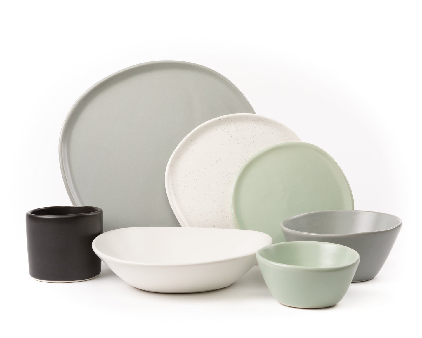 Minimalist ceramic dinnerware set in muted green, gray, white, and black tones with plates, bowls, and a cup