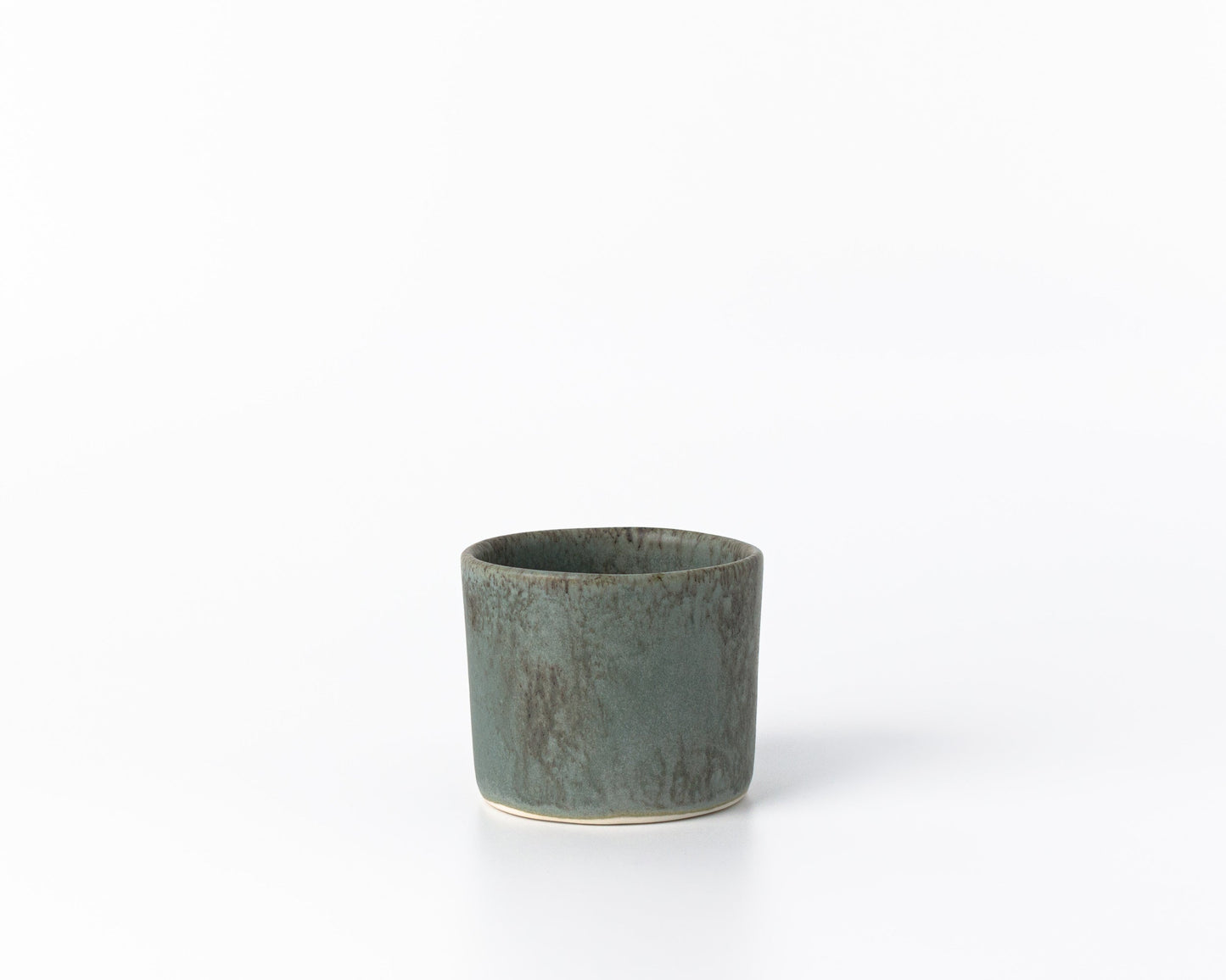Small green ceramic cup with speckled matte finish on white background